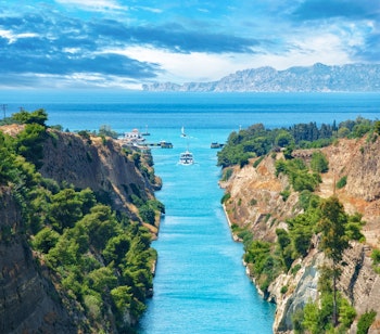 Betagende udsigt over Korinthkanalen med turkisblåt vand, høje klippevægge og en sejlbåd der glider gennem den smalle passage i Grækenland