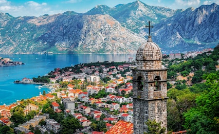 Historisk kirketårn fra Vor Frue af Lindring Kirke med udsigt over Kotors gamle bydel og den smukke bugt omgivet af imponerende bjerge i Montenegro