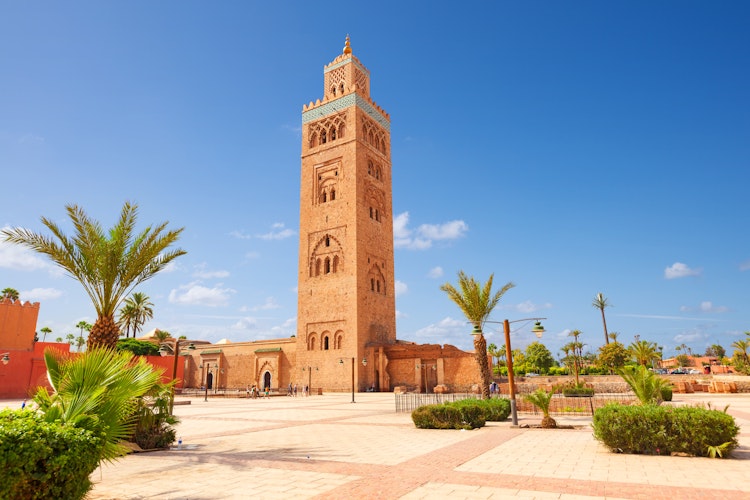 Den berømte Koutoubia-moske i Marrakech med sin imponerende minaret i sandsten, omgivet af palmer under den azurblå marokkanske himmel