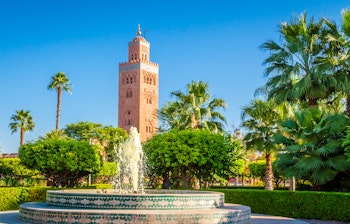 Koutoubia-moskéens minaret i Marrakeshs gamle medina omgivet af haver og palmer, under en klar blå himmel.