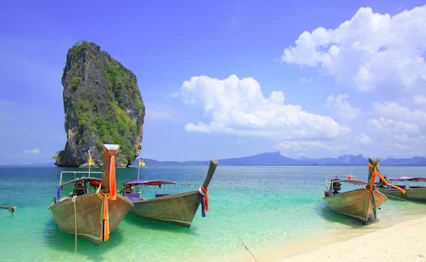 Traditionelle longtail både forankret i krystalklart turkisblåt vand ved Krabi strand Thailand med kalkstensformation