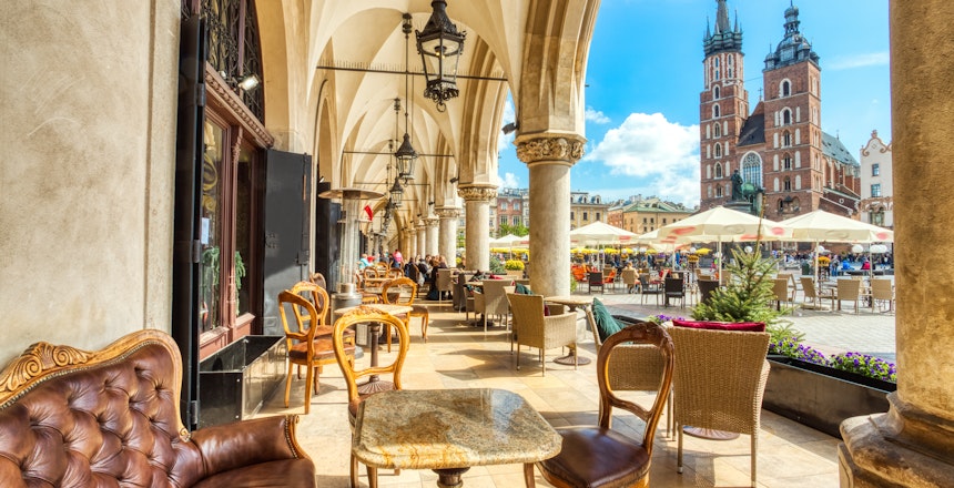 Hyggelig cafe-arkade med udsigt til Mariakirken på Krakows hovedtorv med historisk arkitektur og udendørs spisemuligheder