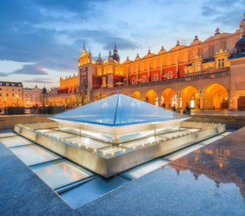 Den oplyste Klædehallen (Sukiennice) på Krakows hovedtorv om aftenen med smukke refleksioner i vand og blå nattehimmel