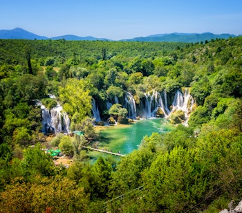Imponerende Kravice-vandfald med turkisblåt vand omgivet af frodig grøn skov i Bosnien-Hercegovina på Balkan