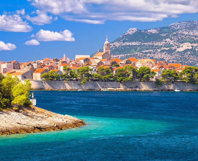 Smuk kroatisk kystby med historiske bygninger, turkisblåt vand og bjerge i baggrunden