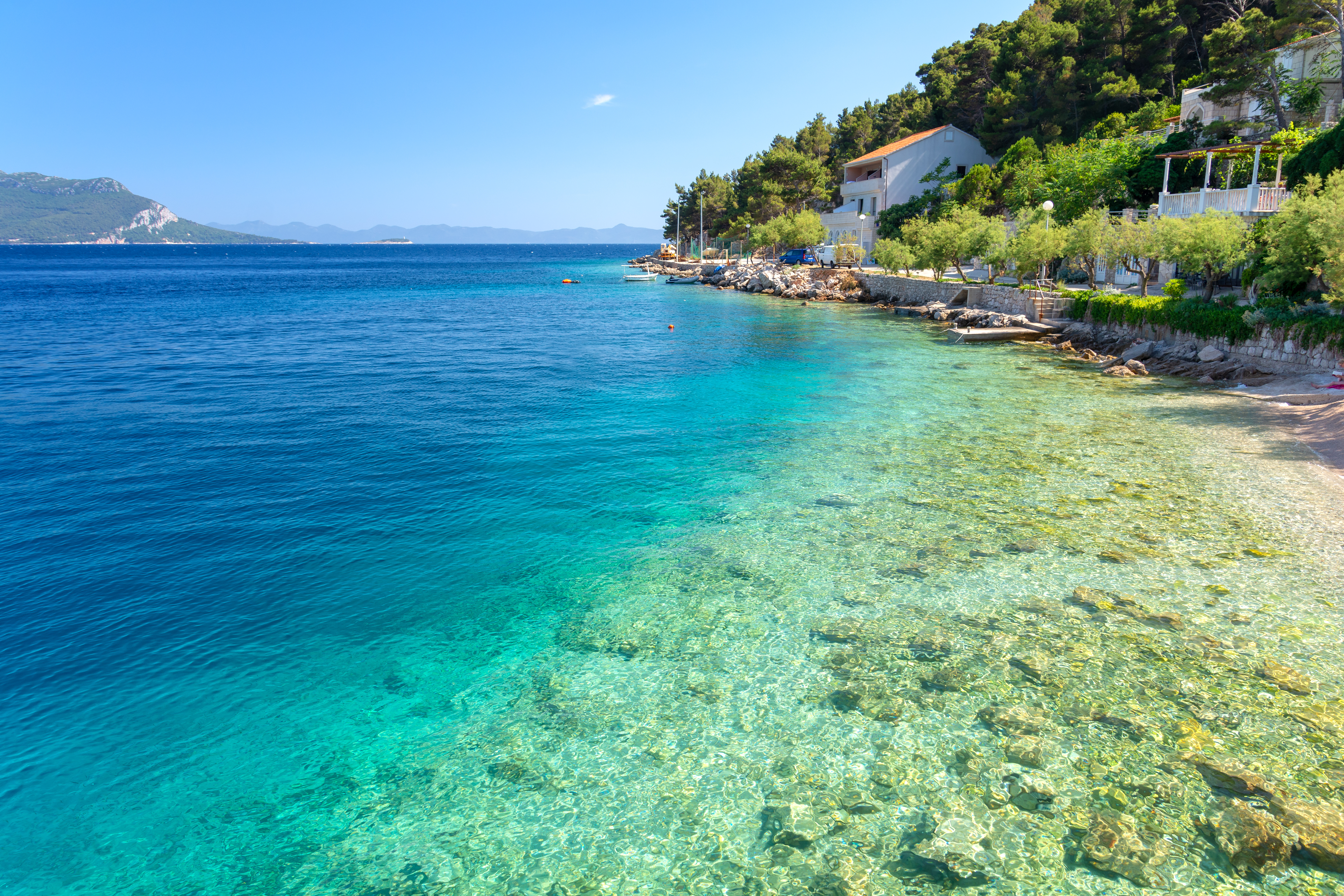 Krystalklart tyrkisblåt vand og smuk strand i kroatisk kystby med middelhavsudsigt