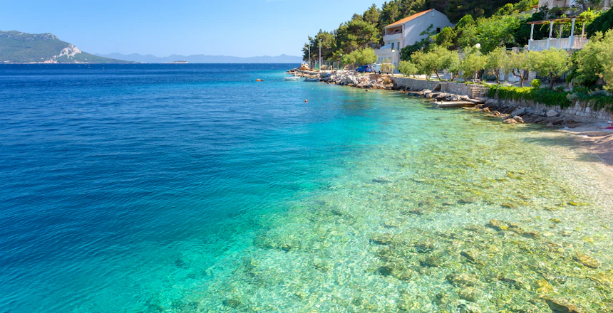 Krystalklart tyrkisblåt vand og smuk strand i kroatisk kystby med middelhavsudsigt