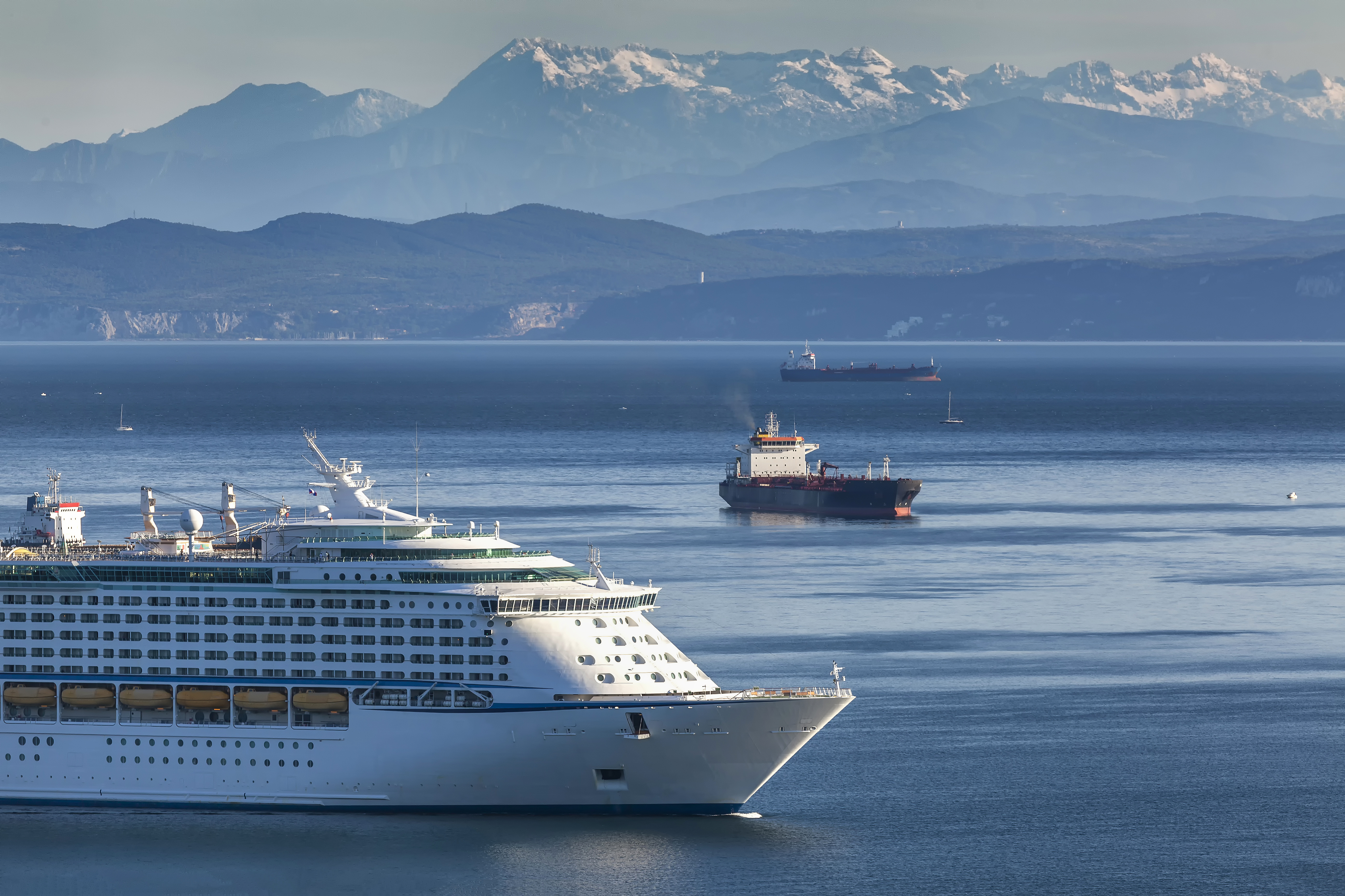 Stort hvidt krydstogtskib ankommer til havnen i Koper, Slovenien med de smukke Juliske Alper i baggrunden og det azurblå hav