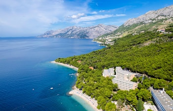 Idyllisk strand med krystalklart vand ved Brela på Makarska Rivieraen i Kroatien, omgivet af grønne pinjetræer og azurblåt hav