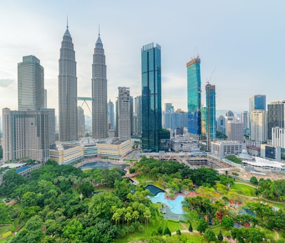 Imponerende luftfoto af Kuala Lumpurs moderne skyline med skyskrabere, der omgiver en frodig grøn bypark under klar blå himmel, Malaysia