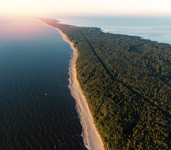 Luftfoto af Kuriske Næs Nationalpark i Litauen med den smukke sandstrand mellem Østersøen og skovklædte klitter ved solnedgang