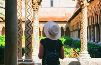 Kvinde med stråhat udforsker den historiske klosterhave ved Monreale Katedralen nær Palermo på Sicilien