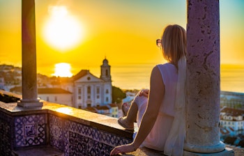 Kvinde nyder den smukke udsigt fra Santa Luzia-udsigtspunktet i Lissabon med solnedgang over Tejo-floden og byens tage