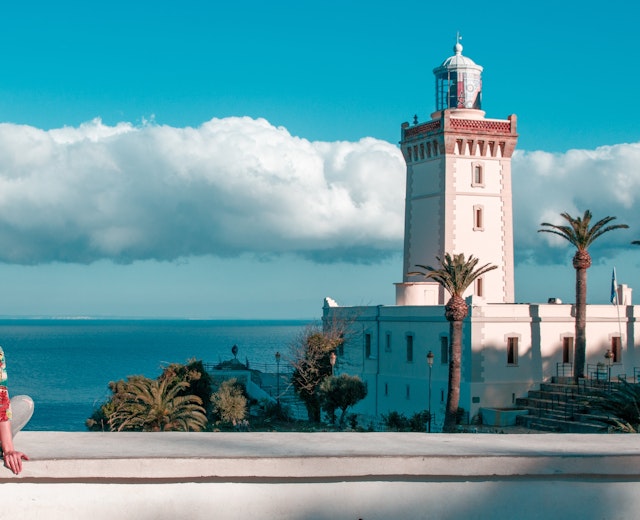 Kvinde nyder udsigten over Cap Spartel fyrtårnet og Middelhavet i Tanger, Marokko under blå himmel