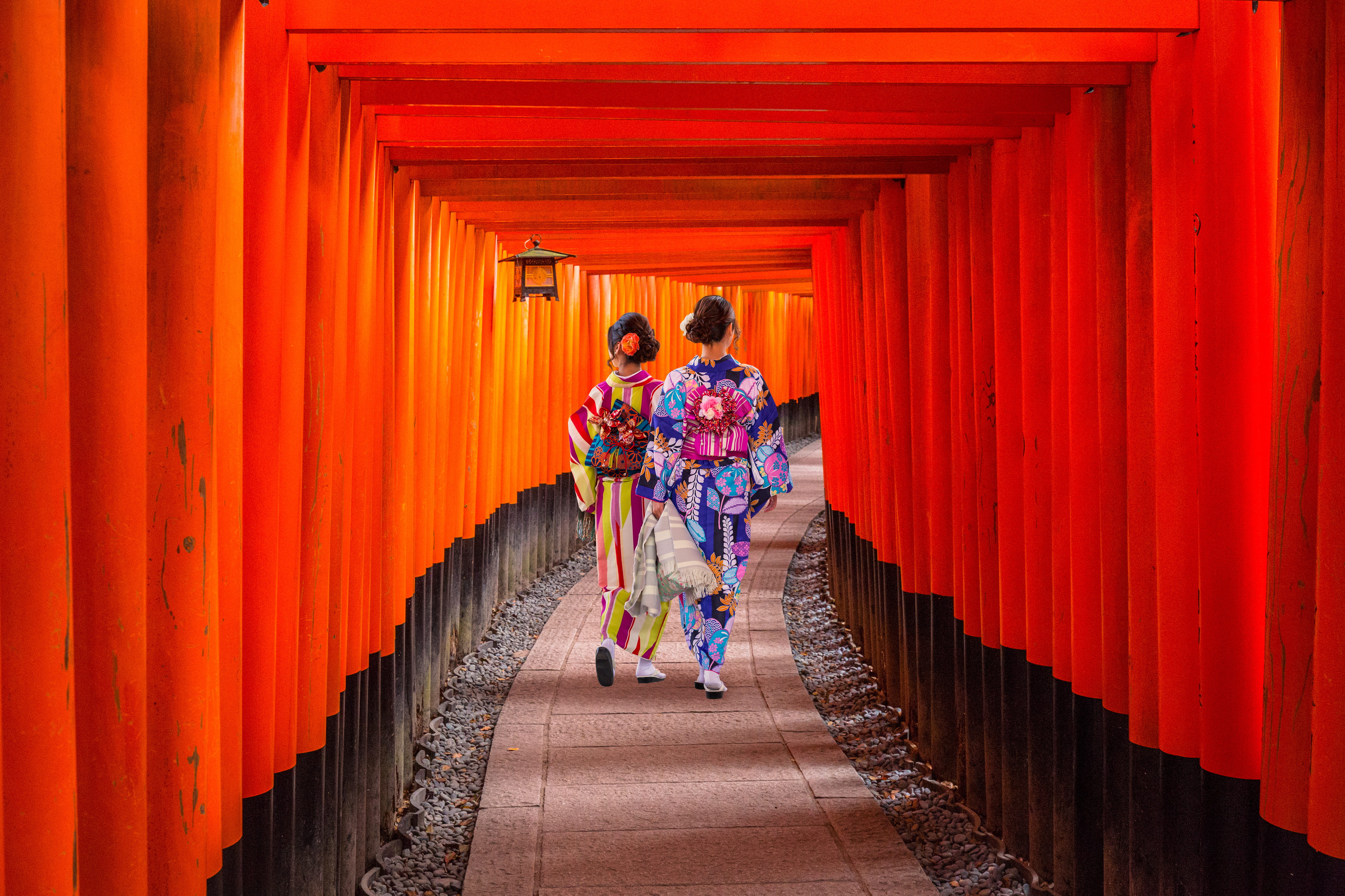 To kvinder i traditionel japansk kimono går gennem orange torii-porte tunnel ved Fushimi Inari helligdom i Kyoto
