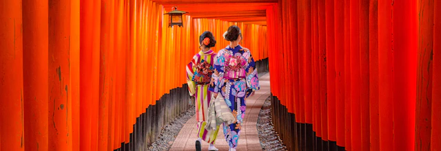 To kvinder i traditionel japansk kimono går gennem orange torii-porte tunnel ved Fushimi Inari helligdom i Kyoto