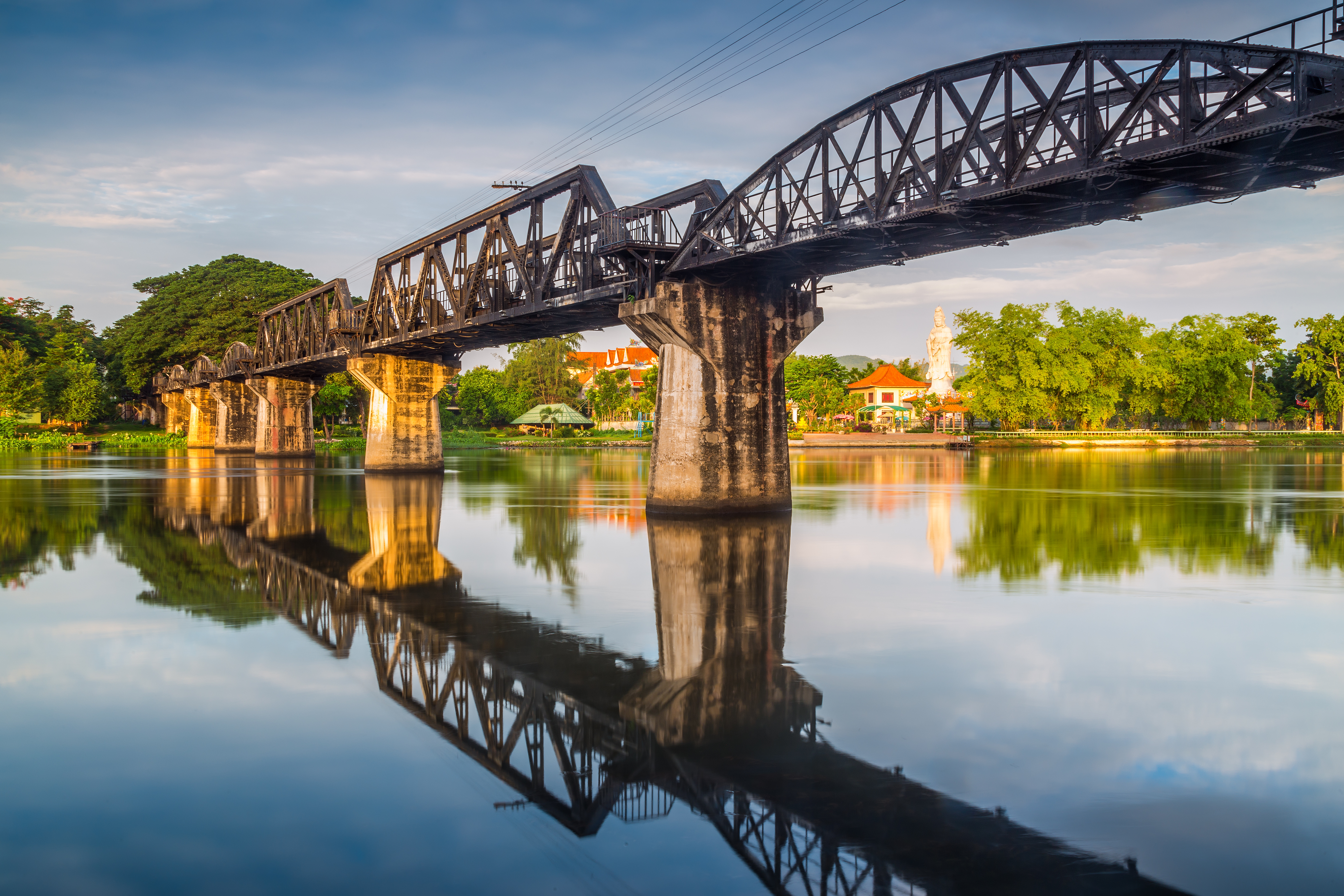 Historiske River Kwai bro i Thailand med smuk afspejling i roligt vand ved solnedgang