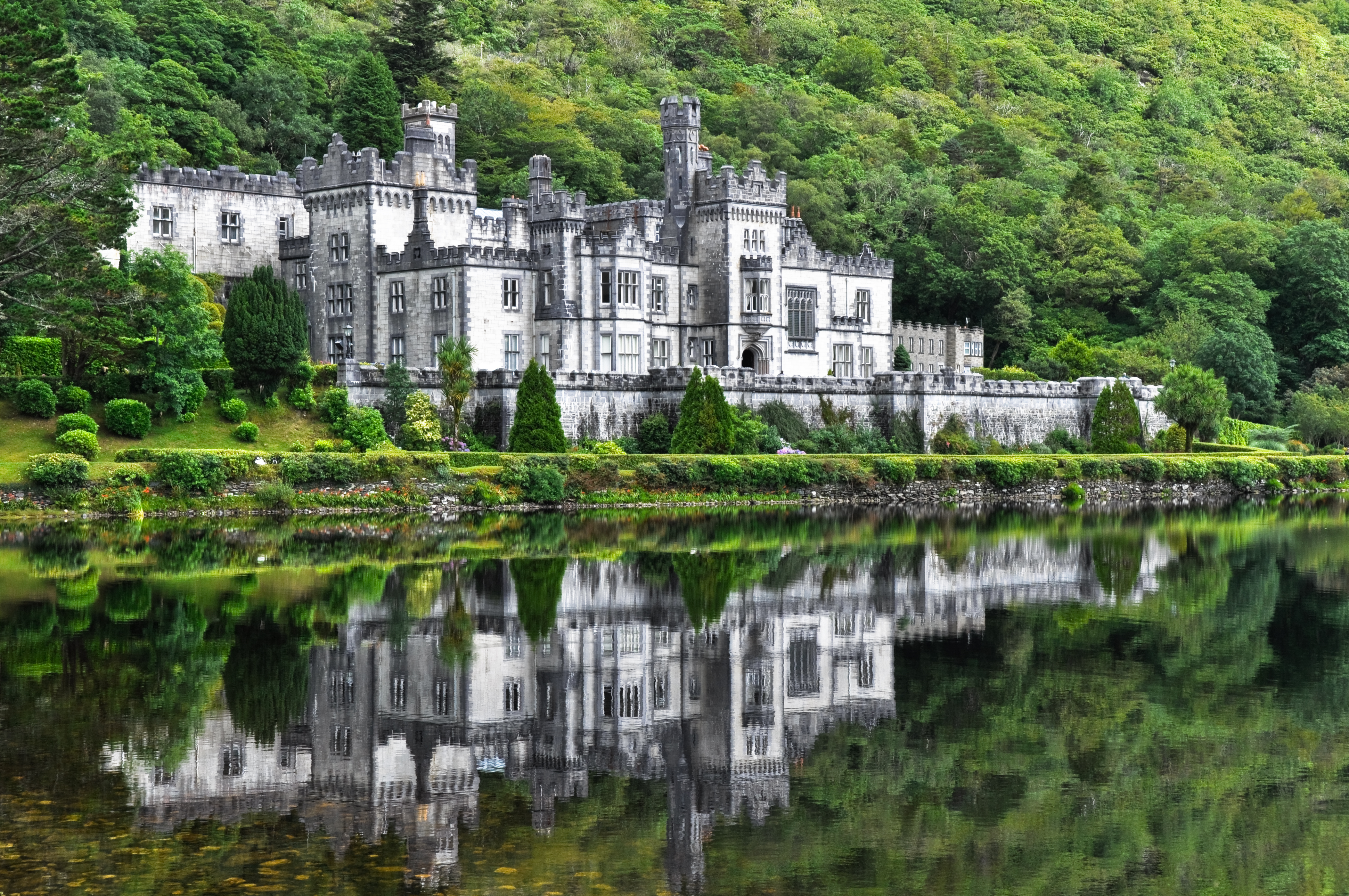 Kylemore Abbey slot spejler sig i fredelig sø omgivet af grønne irske bakker i Connemara