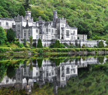 Kylemore Abbey slot spejler sig i fredelig sø omgivet af grønne irske bakker i Connemara
