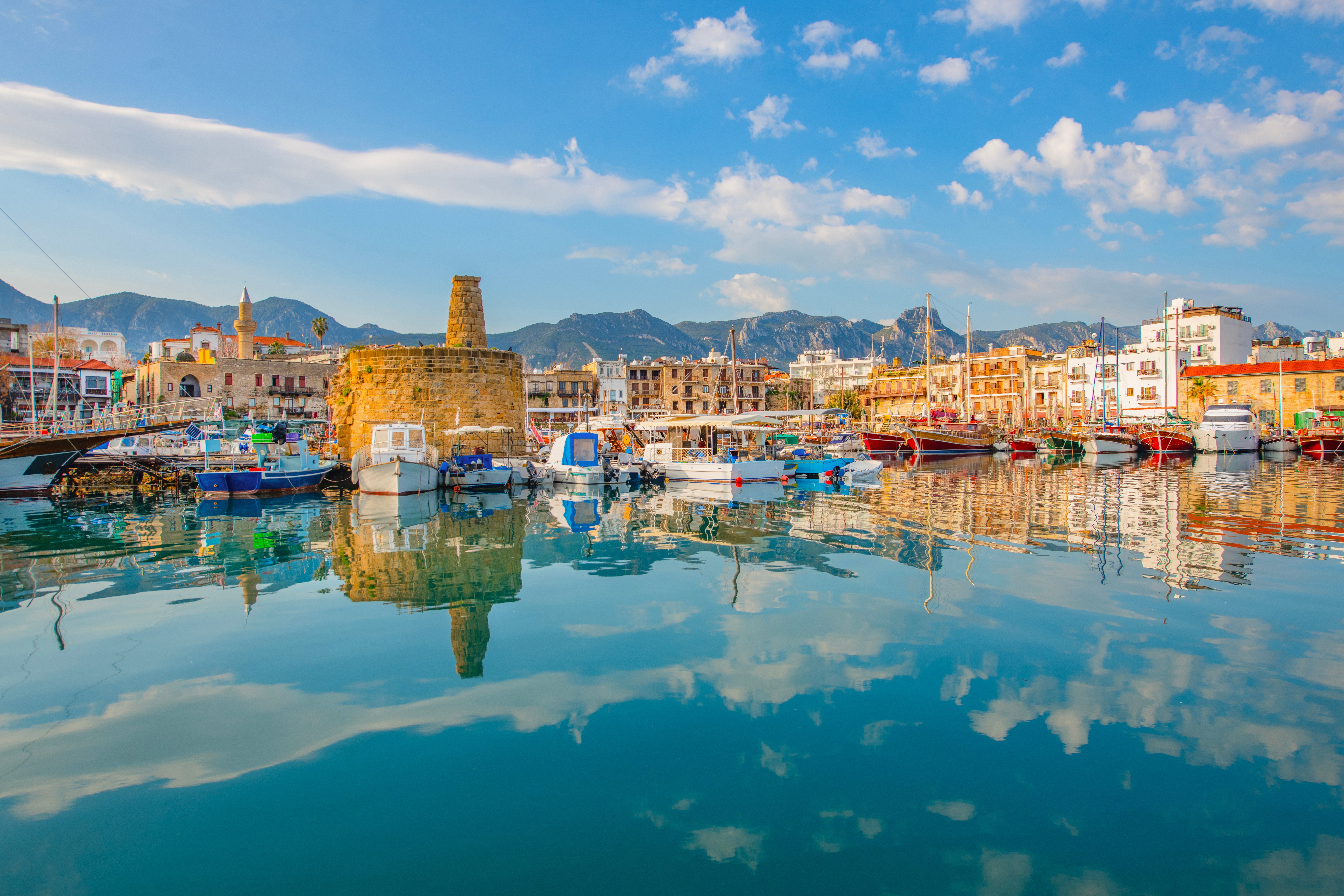 Idyllisk udsigt over Kyrenias gamle havn i Nordcypern med farverige både, historiske bygninger og den middelalderlige fæstning spejlet i det rolige Middelhavs azurblå vand