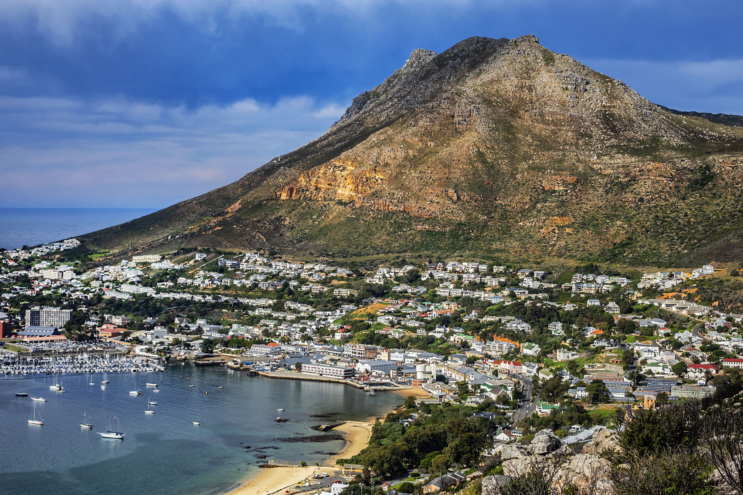 Malerisk kystby med hvide huse ved foden af dramatisk bjerg og turkisblå havneområde
