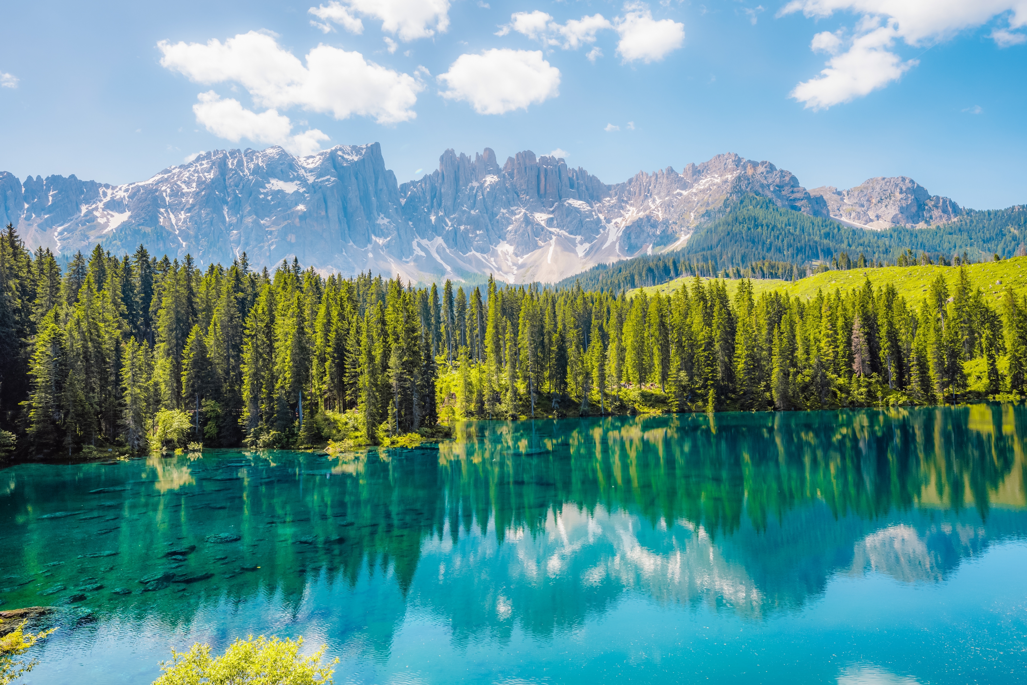 Det turkisblå Lago di Carezza med spejlblankt vand der reflekterer de sneklædte Dolomit-bjerge og tæt nåleskove i Sydtyrol, Italien