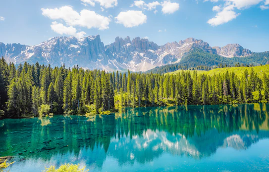 Det turkisblå Lago di Carezza med spejlblankt vand der reflekterer de sneklædte Dolomit-bjerge og tæt nåleskove i Sydtyrol, Italien