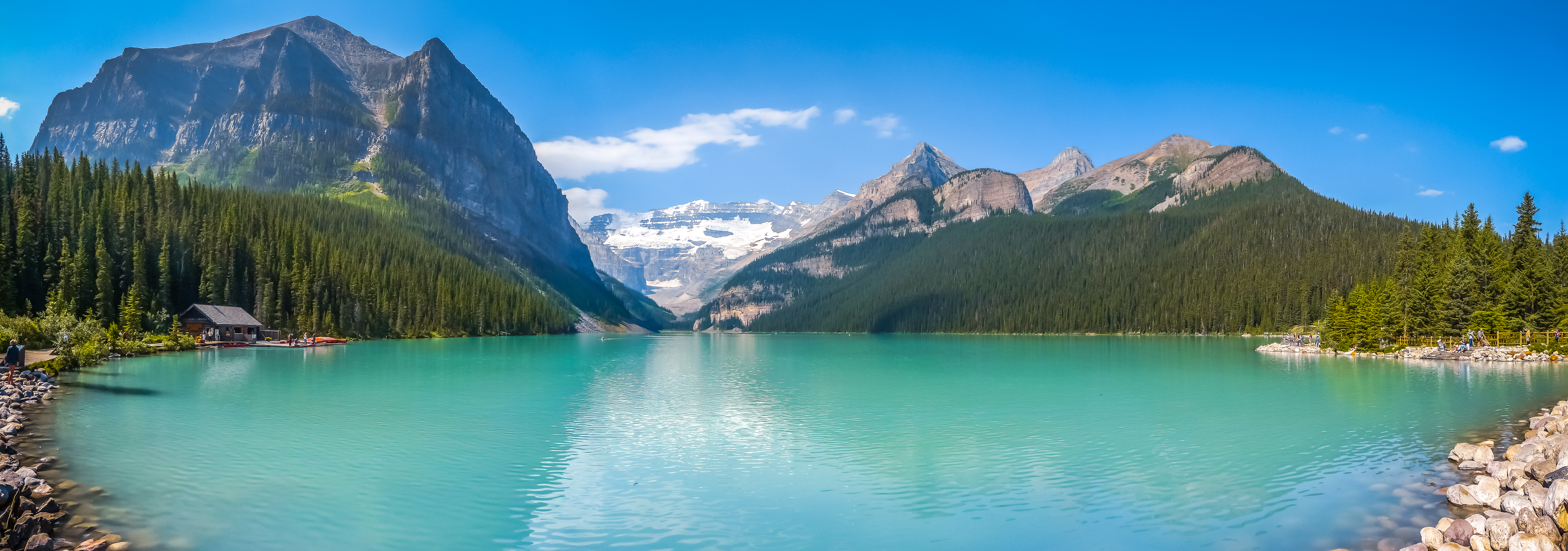 Betagende panoramaudsigt over Lake Louise med sit ikoniske turkisblå vand omgivet af majestætiske sneklædte bjerge og frodig nåleskov i Banff National Park, Alberta, Canada
