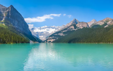 Betagende panoramaudsigt over Lake Louise med sit ikoniske turkisblå vand omgivet af majestætiske sneklædte bjerge og frodig nåleskov i Banff National Park, Alberta, Canada