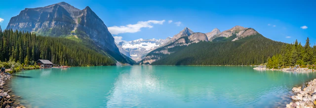 Betagende panoramaudsigt over Lake Louise med sit ikoniske turkisblå vand omgivet af majestætiske sneklædte bjerge og frodig nåleskov i Banff National Park, Alberta, Canada