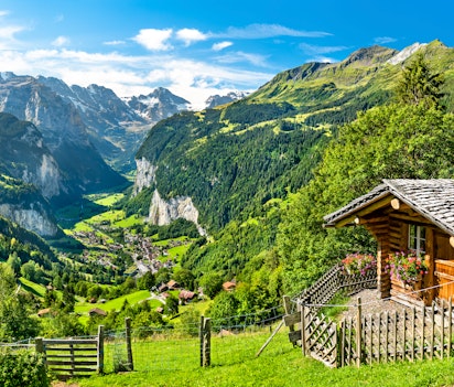 Betagende panoramaudsigt over Lauterbrunnen-dalen set fra Wengen i de schweiziske alper, med frodige grønne enge og dramatiske sneklædte bjerge under en klar blå himmel i dette UNESCO-anerkendte alpelandskab