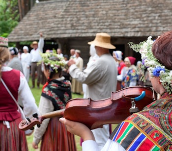 Lettiske folkedansere og musikere i farverige traditionelle dragter optræder ved en sommerlig kulturfestival på landet i Letland