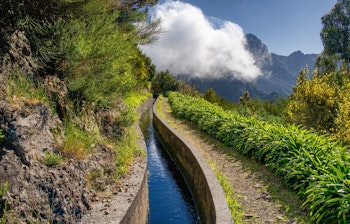 Idyllisk vandingskanal Levada do Norte med vandresti der snor sig gennem det frodige bjerglandskab på Madeira i Portugal