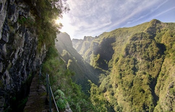 Naturskøn levada-vandrerute med rækværk gennem en frodig grøn dal på Madeira, perfekt til vandreferie i bjerglandskab