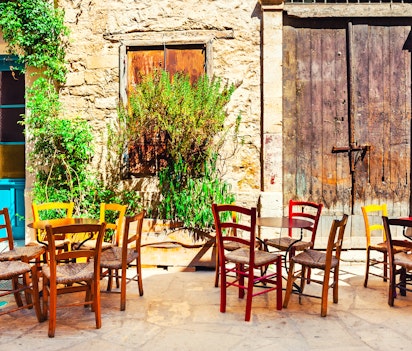 Hyggelig udendørs café med farverige borde og stole på en malerisk gammel gade i Limassol, Cypern, der indfanger den autentiske middelhavsstemning og lokale kultur på denne charmerende ø