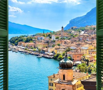 Smuk udsigt gennem grønne skodder over Limone sul Garda ved Gardasøen med farverige bygninger og bjerge i Lombardiet, Italien