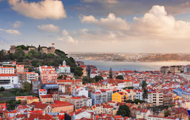 Malerisk udsigt over Lissabons historiske bymidte med traditionelle portugisiske bygninger badet i gyldent aftenlys, med udsigt over Tagus-floden ved solnedgang