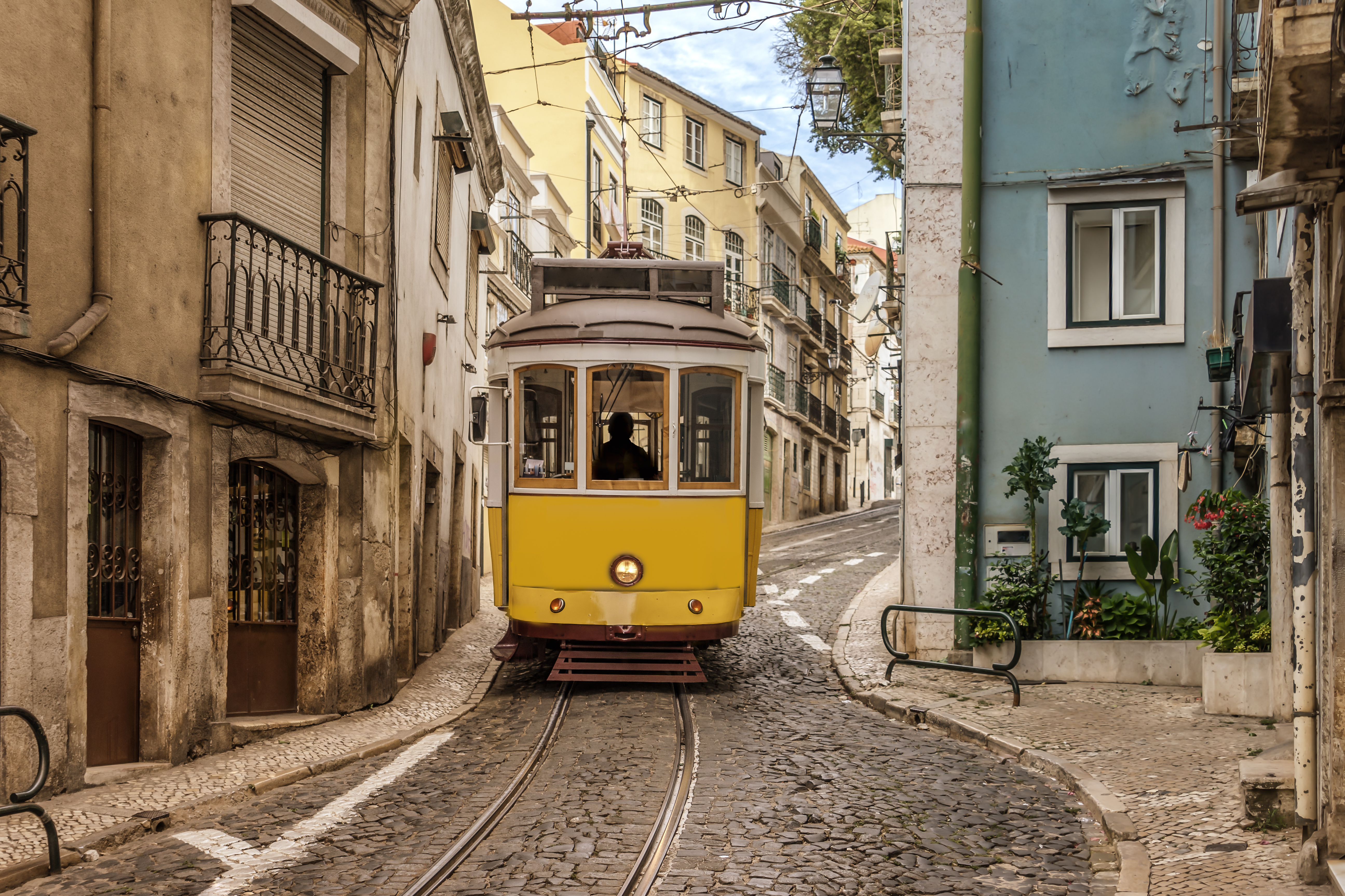 Historisk gul sporvogn kører gennem smalle brolagte gader i Lissabons gamle Alfama-kvarter med traditionel portugisisk arkitektur