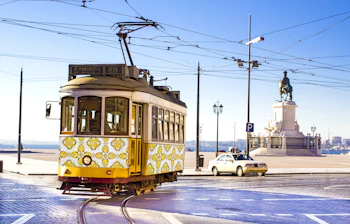 Klassisk gul sporvogn kører gennem Praça do Comércio (Handelspladsen) i centrum af Lissabon, et ikonisk symbol på byens charmerende offentlige transportsystem