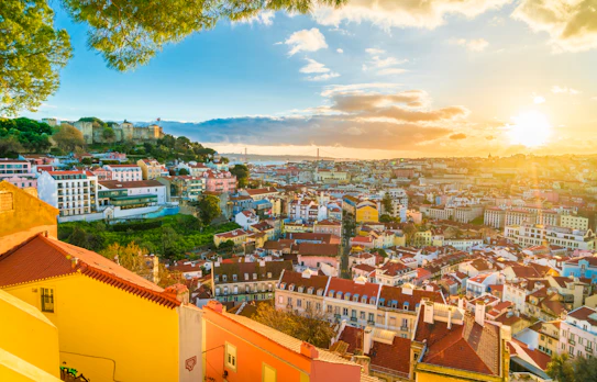 Betagende panoramaudsigt over Lissabons historiske bylandskab med Alfama-kvarteret og São Jorge-slottet badet i solnedgangens gyldne lys