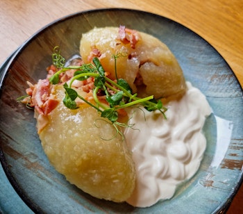 Traditionel litauisk cepelinai - kartoffelboller fyldt med kød, serveret med flødesauce og bacon på en dekorativ tallerken
