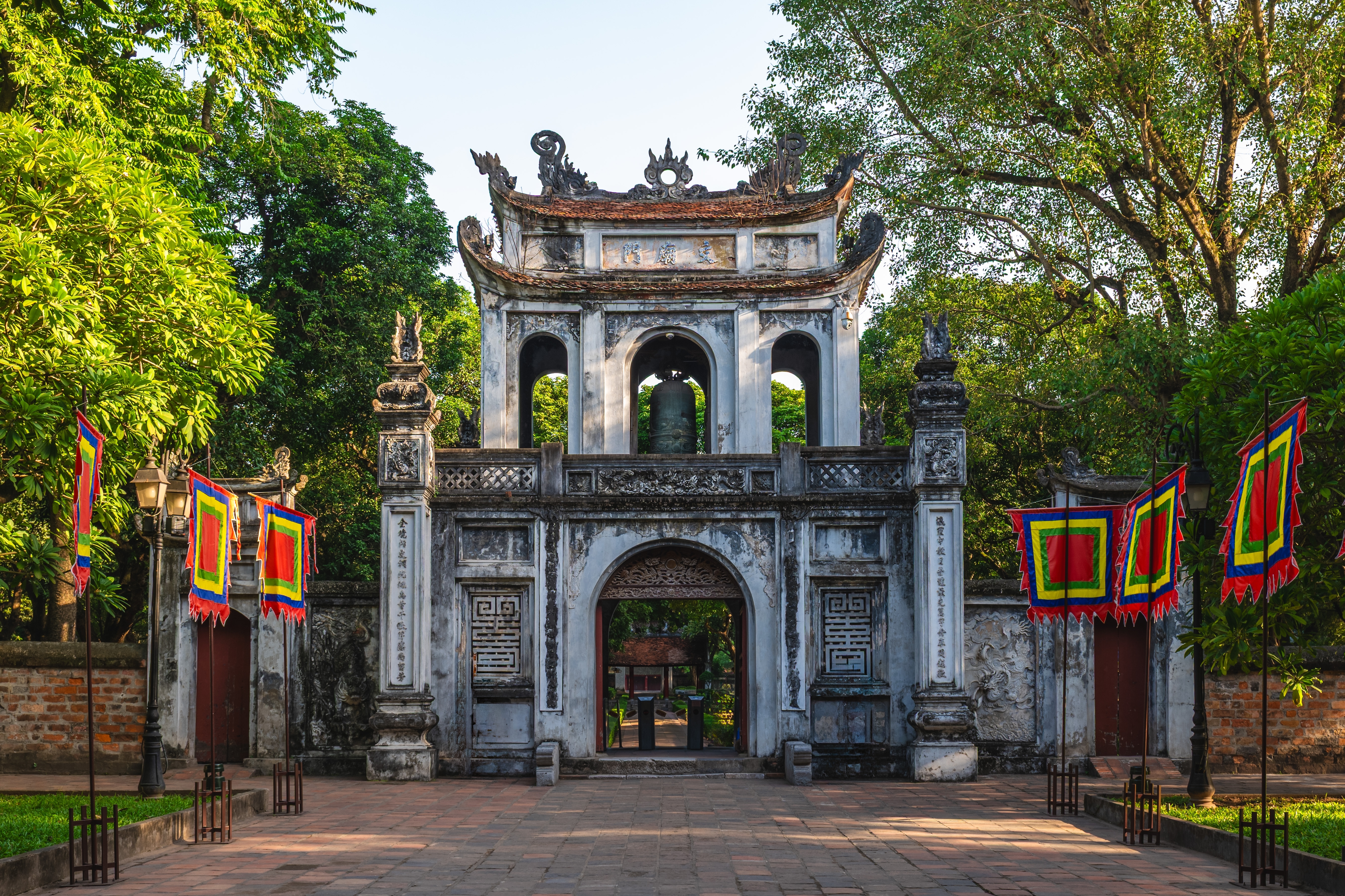 Den historiske stenport ved Litteraturens Tempel i Hanoi, Vietnam, prydet med farverige traditionelle flag og detaljerede udskæringer
