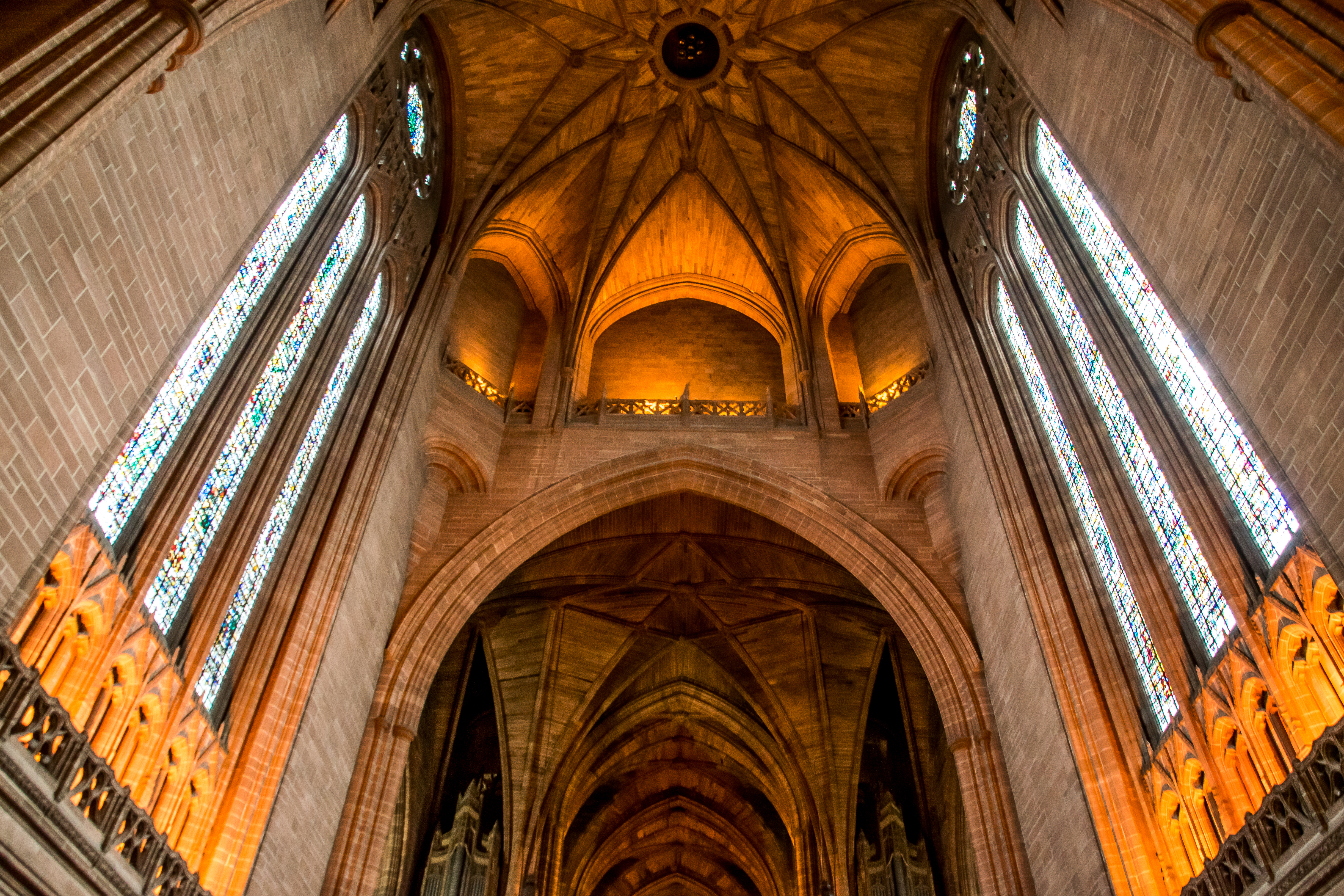 Imponerende indre af Liverpool Katedralen med høje gotiske buer, farverige glasmosaikvinduer og majestætisk hvælvet loft badet i gyldent lys