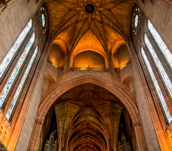 Imponerende indre af Liverpool Katedralen med høje gotiske buer, farverige glasmosaikvinduer og majestætisk hvælvet loft badet i gyldent lys