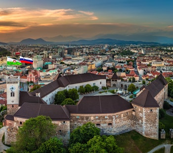 Panoramisk luftfoto af Ljubljana Slot og byens historiske centrum ved solnedgang med Franciskanerkirken og Ljubljana Katedral i Sloveniens hovedstad