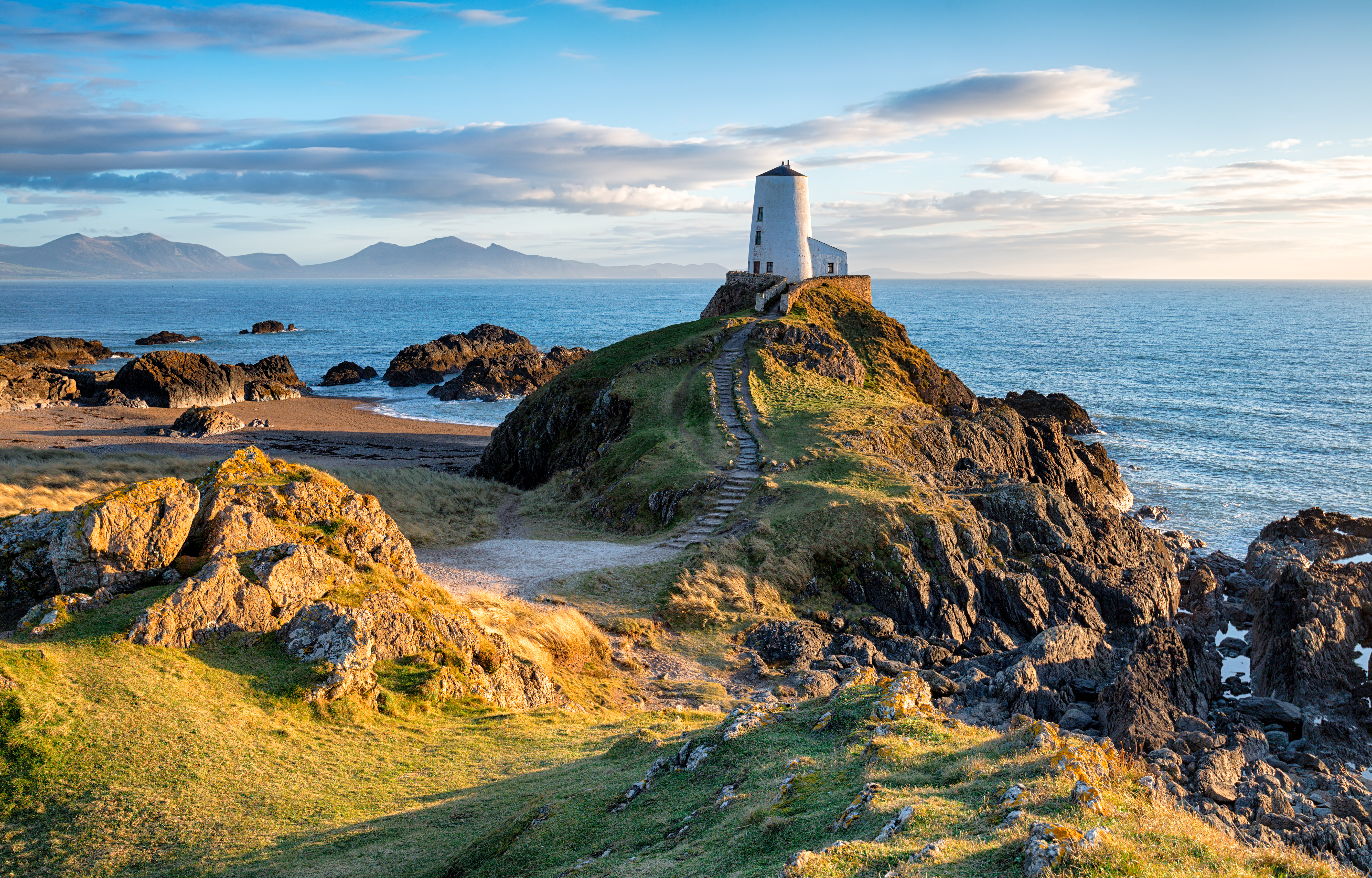 Malerisk fyrtårn på Llanddwyn Island ved Newborough på Anglesey-kysten i Wales. Dramatisk kystlandskab med klippeformationer og blåt hav under skyet himmel