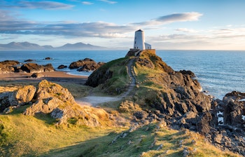 Malerisk fyrtårn på Llanddwyn Island ved Newborough på Anglesey-kysten i Wales. Dramatisk kystlandskab med klippeformationer og blåt hav under skyet himmel