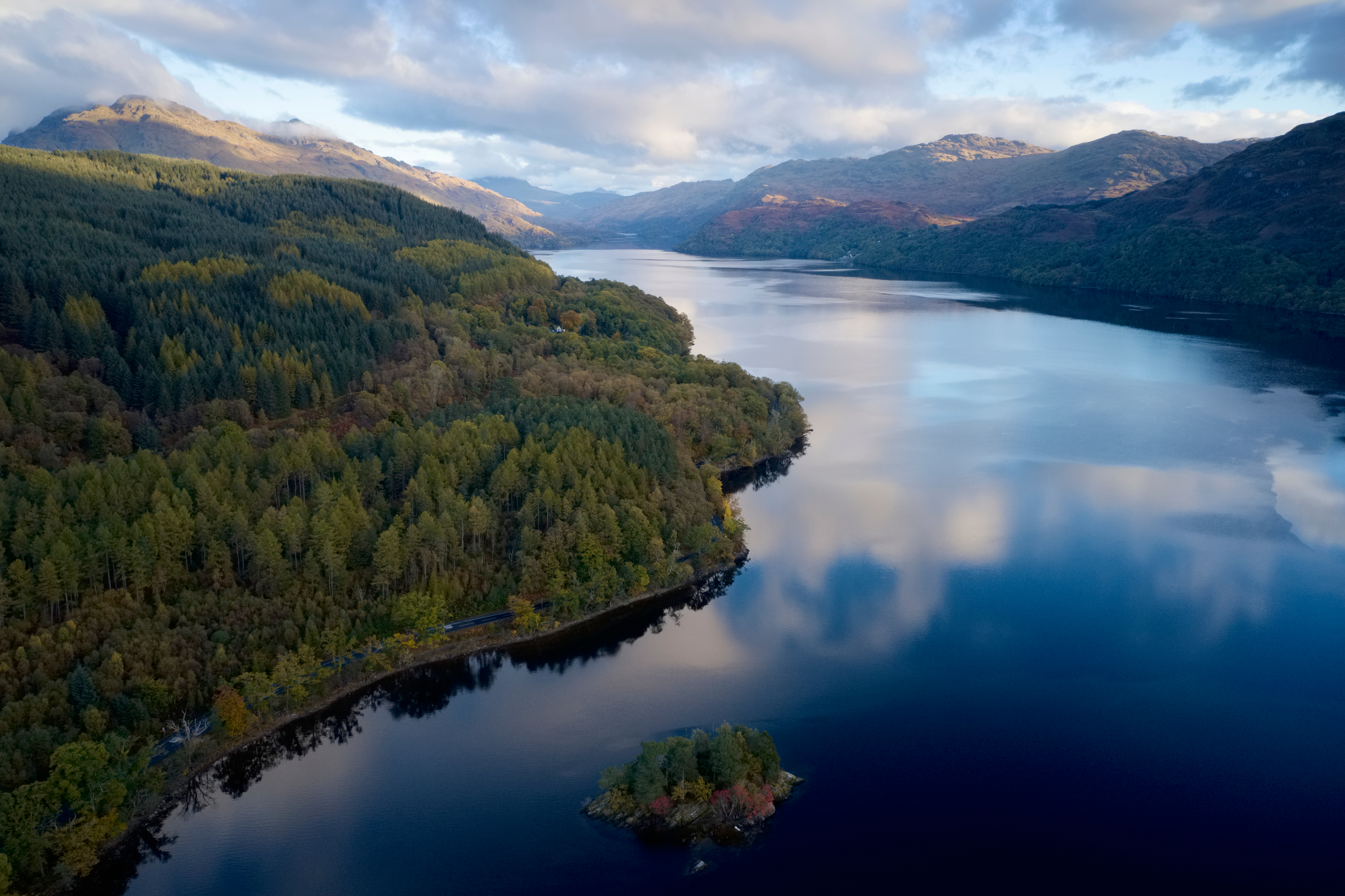 Luftfoto af Loch Lomond i Skotland med efterårsfarver og bjerglandskab spejlet i det stille vand
