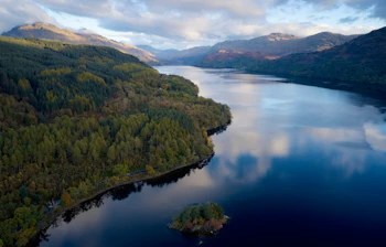 Luftfoto af Loch Lomond i Skotland med efterårsfarver og bjerglandskab spejlet i det stille vand