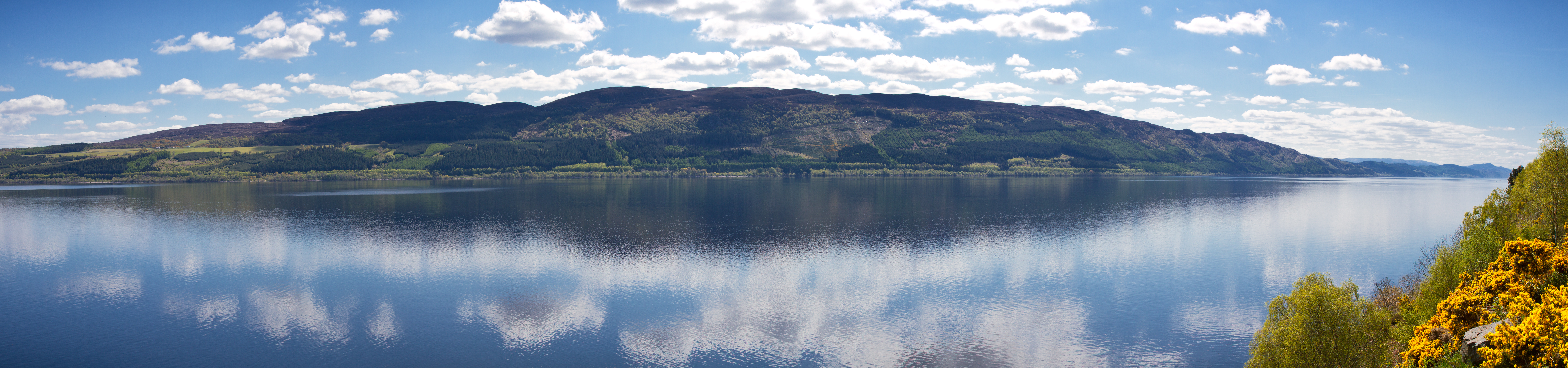 Panoramaudsigt over Loch Ness med perfekte skyrefleksioner på det rolige vand i de skotske højlande
